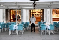 FILE - A bar employee wears a protective face mask while standing at St. Mark's Square amid the coronavirus disease (COVID-19) outbreak in Venice, Italy July 9, 2020.