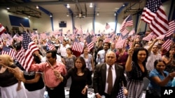 FILE - People hold flags as they are sworn in as U.S. citizens during a naturalization ceremony in Phoenix, Arizona.
