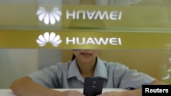 A sales assistant looks at her mobile phone as she waits for customers behind a counter at a Huawei booth in Wuhan, Hubei province, China.