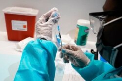 FILE- A health care worker fills a syringe with the Pfizer COVID-19 vaccine, at the American Museum of Natural History in New York, July 22, 2021.