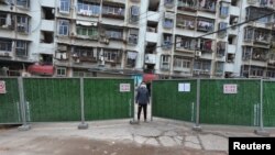 FILE - A man wearing a face mask keeps watch at an entrance to a residential community that has been fenced in with temporary barriers, in Yichang city of Hubei, the province hit hardest by the novel coronavirus outbreak, Feb. 10, 2020.