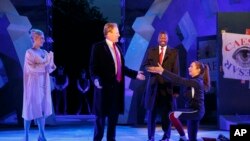 In this May 21, 2017 photo provided by The Public Theater, Tina Benko, left, portrays Melania Trump in the role of Caesar's wife, Calpurnia, and Gregg Henry, center left, portrays President Donald Trump in the role of Julius Caesar during a dress rehearsa