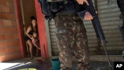 A woman moves her baby inside while a soldier patrols during an operation at the Rocinha slum, in Rio de Janeiro, Brazil, Oct. 10, 2017. 