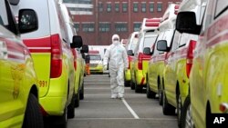 Radnik u zaštitnom odelu pored vozila za prevoz pacijenata obolelih od koronavirusa u Južnoj Koreji