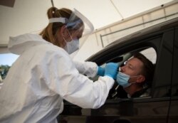 A health care worker demonstrates a nasal swab on a patient during a test day at a drive-thru COVID-19 testing site in Antwerp, Belgium, Aug. 5, 2020.