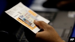 FILE - An election official checks a voter's photo identification at an early voting polling site in Austin, Texas, Feb. 26, 2014. 