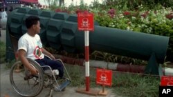 ជន​រងគ្រោះ​ពិការ​ដោយ​គ្រាប់​មីន​ម្នាក់​ ពិនិត្យ​មើល​ស្តូប​ជា​រូប​គ្រាប់​មីន​​នៅ​សាល​សន្នីសីទ​ចតុមុខ​ក្នុង​ក្រុង​ភ្នំពេញ​កាល​ពី​ថ្ងៃ​អង្គារ​ទី​២៤​ខែ​កុម្ភៈ​ឆ្នាំ​១៩៩៨។