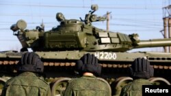 FILE - Russian tank crew members wait for their T-72B tank to be ready to move off a train shortly after Russian tanks arrived at a train station in the Crimean settlement of Gvardeiskoye.
