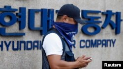 Seorang karyawan Hyundai Motor berdiri di depan logo perusahaan pembuat mobil tersebut di pabrik mereka di Asan, selatan Seoul (Foto: dok). Sekitar 40 ribu karyawan Hyundai Motor Co.kembali mogok kerja, memrotes keputusan perusahaan untuk mengeluarkan dana $10 milyar untuk membeli lahan bagi pendirian kantor baru.