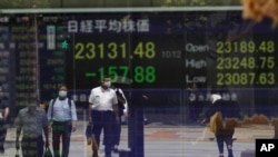 Orang-orang menunggu di persimpangan lalu lintas, tercermin pada monitor yang menunjukkan indeks Nikkei 225 Jepang di sebuah perusahaan sekuritas di Tokyo pada hari Senin, 17 Agustus 2020. (Foto: AP)
