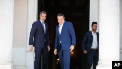 Greece's newly-elected prime minister Kyriakos Mitsotakis (L) looks on as outgoing prime minister Alexis Tsipras, center,leaves the Maximos Mansion in Athens,, July 8, 2019.
