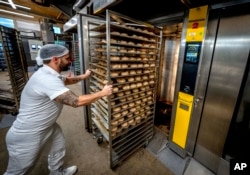 An employee pushes bread rolls into one of the gas heated ovens in the producing facility in Cafe Ernst in Neu Isenburg, Germany, Monday, Sept. 19, 2022. Andreas Schmitt, head of the local bakers' guild, said some small bakeries are contemplating giving up due to the energy crisis. (AP Photo/Michael Probst)