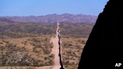 FILE - In this May 19, 2021 photo the border wall stretches along the landscape near Sasabe, Ariz. The bodies of an unusually large number of migrants who died in Arizona's borderlands are being recovered this summer amid record temperatures.