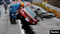 Spasilac gleda u automobil zarobljen u pukotini na putu nastaloj tokom zemljotresa u blizini Anamiza, Japan, 3. januara 2023.