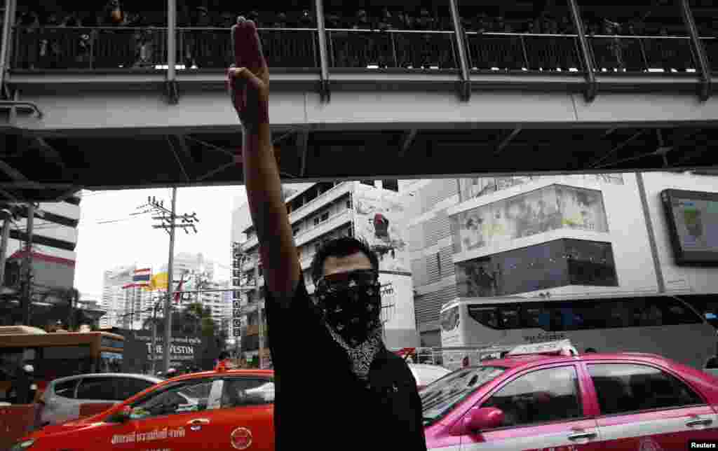 A protester against military rule gestures by holding up his three middle fingers in the air, as soldiers look on from an elevated walkway, during a brief demonstration outside a shopping mall in Bangkok, June 1, 2014. 
