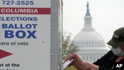With the U.S. Capitol dome visible, a voter drops a ballot into an early voting drop box, Oct. 28, 2020, at Union Market in Washington. 