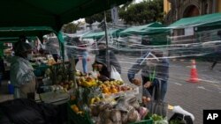 Women buy vegetables through a protective plastic due to COVID-19, in a street market in Barranco neighborhood, in Lima, Peru, Saturday, June 20, 2020.