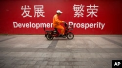 2015年7月15日北京市中心的一条街道上，一名维修工人骑着摩托车经过用中英文写着“发展”和“繁荣”的横幅