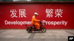 FILE - A maintenance worker rides a scooter past banners reading "Development" and "Prosperity" in English and Chinese on a street in central Beijing, July 15, 2015.