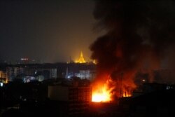 Smoke rises from a fire at Ruby Mart in Yangon in the early morning of April 1, 2021 with the Shwedagon Pagoda seen illuminated in the background, as the country continues to be in turmoil after the February military coup. (Photo by STR / AFP)