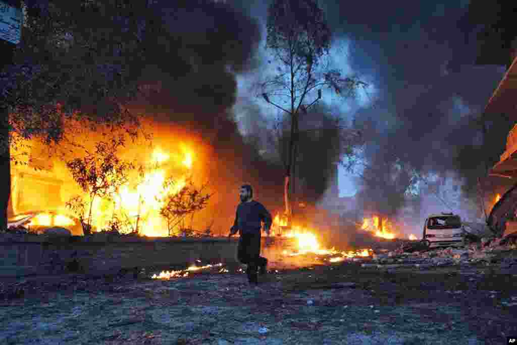 This picture provided by the anti-government activist group Coordination Committee In Kfar Takharim shows a Syrian man running as flames rise from buildings which were attacked by a Syrian air strike in Kfar Takharim, March 1, 2014. 