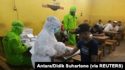 Petugas medis yang mengenakan alat pelindung mengambil sampel darah dari pengunjung yang dites virus corona di Surabaya, provinsi Jawa Timur, 18 April 2020. (Foto: Antara/Didik Suhartono) via Reuters)