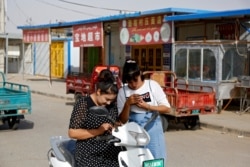 In this Sept. 20, 2018 photo, Uighur women look at their smartphones near restaurants and shophouses operated by Uighurs at the Unity New Village in Hotan, in western China's Xinjiang region.