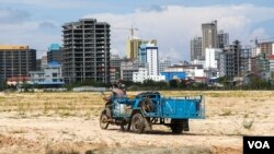 រូបឯកសារ៖ បុរសម្នាក់បើកម៉ូតូអូសរទេះដឹកអីវ៉ាន់ កាត់ផ្លូវក្រោយសំណង់អគារខ្ពស់ស្កឹមស្កៃ នៅខេត្តព្រះសីហនុ កាលពីថ្ងៃទី ៥ ខែតុលា ឆ្នាំ ២០២១។ (ស៊ុន ណារិន/វីអូអេ)