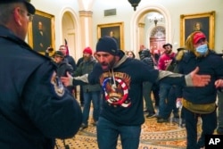 FILE - Mtu akiwa amevaa fulana yenye maandishi QAnon akikabiliana na afisa polisi wa Bunge la Marekani ndani ya Baraza la Seneti Washington, Jan. 6, 2021.