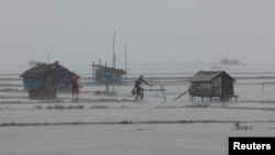 People walk along shrimp and crab farms that are flooded due to heavy rain as Cyclone Remal passes the country, in the Shyamnagar area of Satkhira, Bangladesh, May 27, 2024.
