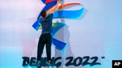 FILE - A crew member leaps to fix a logo for the 2022 Beijing Winter Olympics before a launch ceremony to reveal the motto for the Winter Olympics and Paralympics in Beijing, Sept. 17, 2021.