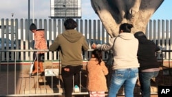 (File) In this Jan. 8, 2020, photo, people seeking asylum in the United States wait at the border crossing bridge in Tijuana, Mexico, just across the border from San Diego.