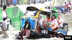 Warga mengunakan 'tuk-tuk', semacam becak di Bangkok, untuk melintasi jalanan yang tergenang banjir (7/11).