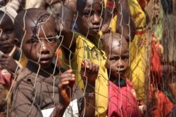 FILE - Burundian children, who fled their country, stand behind a fence at Nyarugusu camp, Tanzania, June 11, 2015.