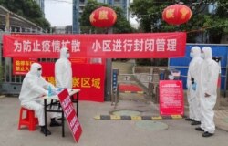 FILE - Workers in protective suits are seen at a checkpoint for registration and body temperature measurement, at an entrance to a residential compound in Wuhan, in Hubei province, China, Feb. 13, 2020.