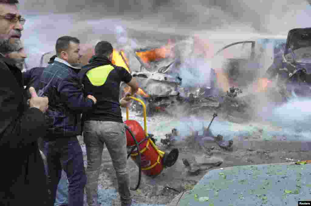 Civil Defense members move a fire extinguisher as a Hezbollah member carries a walkie-talkie at the site of an explosion in Haret Hreik, Beirut, Jan. 21, 2014.