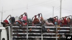 FILE - Garment workers stand on the cargo platform of a truck as they head home after their work shift outside Phnom Penh, Cambodia, Nov. 11, 2020. 
