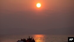 File - In this Sunday, March 20, 2016, file photo, the sun rises as migrants and refugees on a dingy arrive at the shore of the northeastern Greek island of Lesbos, after crossing the Aegean sea from Turkey.