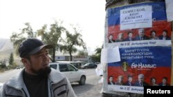Seorang penduduk setempat memperhatikan poster kampanye pemilu, di desa Vorontsovka dekat ibukota Bishkek, Kyrgyzstan, 1 Oktober 2015. (REUTERS/Vladimir Pirogov)