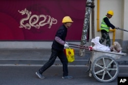 Para pekerja mendorong troli yang lewat di toko ritel yang sedang dibangun yang memamerkan patung berbentuk naga 2024, Tahun Naga dalam kalender China, di Shanghai, China pada 25 November 2023. (Foto: AP)