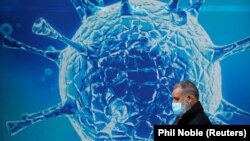 Great Britain, A man wearing a protective face mask walks past an illustration of a virus outside a regional science centre