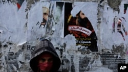 FILE - A Bahraini anti-government protester watches for riot police from in front of a wall with posters of a Shiite cleric executed in Saudi Arabia and other opposition posters that have been torn by authorities in Sitra.
