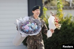 Anggota boy band K-pop BTS, J-Hope, tersenyum sambil memegang bunga setelah menyelesaikan wajib militer selama 18 bulan di luar pangkalan militer di Wonju, Korea Selatan, 17 Oktober 2024. (Foto: Reuters)