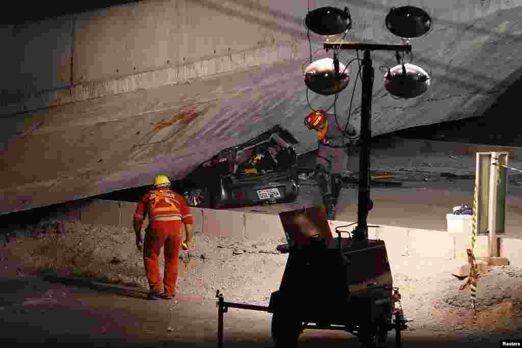 Rescue workers inspect a car trapped underneath a bridge that collapsed while under construction in Belo Horizonte, July 3, 2014.