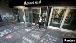 FILE PHOTO: A woman exits Mount Sinai Hospital in Manhattan past messages of thanks written on the sidewalk during the outbreak of the coronavirus disease (COVID19) in New York City, New York, April 7, 2020.