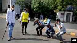 An Indian policeman, left and a civil defense person, second left, make people perform sit ups while holding their ear lobes, as a punishment for stepping out without a valid reason during a lockdown in Ahmedabad, India, Tuesday, March 24, 2020. 