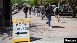 People walk past a bilingual sign directing voters to a polling place at the Arizona State University Downtown Campus A.E. England building as the Democratic and Republican parties hold primary elections in Phoenix, Arizona, March 19, 2024. 