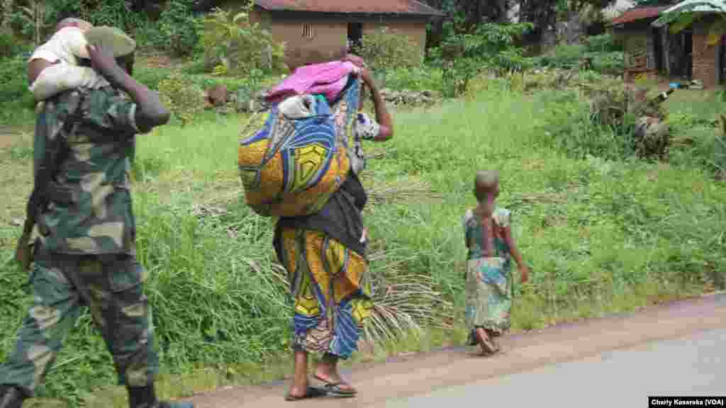 Un soldat, kalachnikov en bandoulière, un enfant sur ses épaules, marche derrière une femme et un enfant près d&rsquo;un camp de déplacés à OICHA, Beni, 28 octobre&nbsp; 2015 (Charly Kasereka/VOA).