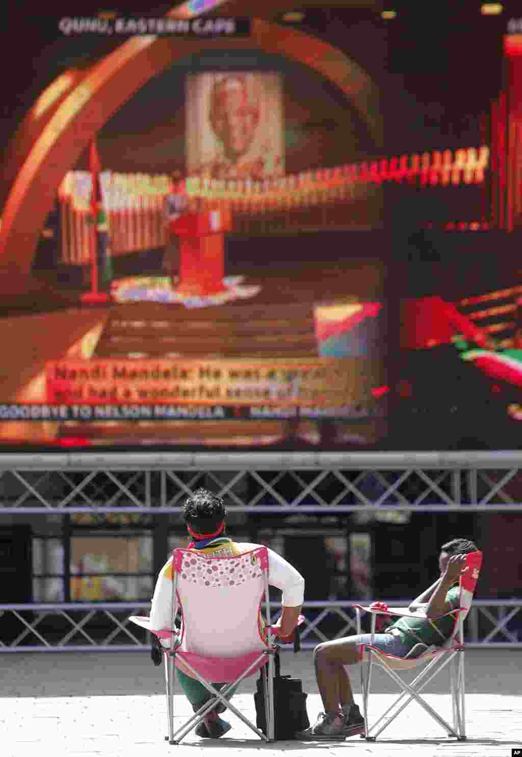Two people follow the proceedings of Nelson Mandela&#39;s funeral on a big screen in Nelson Mandela square in Sandton, Johannesburg.