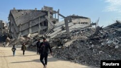 গাজায় ধ্বংস হয়ে যাওয়া বাড়ি ও দালানের ধ্বংসাবশেষের মধ্য দিয়ে হেঁটে যাচ্ছেন ফিলিস্তিনিরা। 